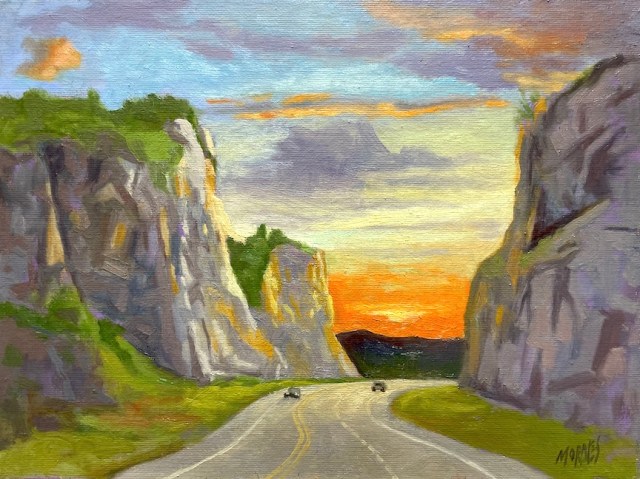 Pintura de un paisaje al atardecer, con montañas a los lados de una carretera que se extiende hacia el horizonte, donde se ve un colorido cielo con nubes y un sol poniente.