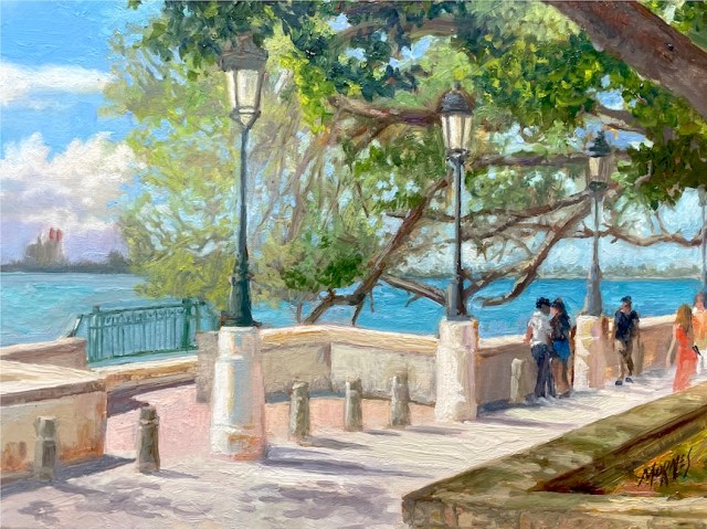 Vista de un paseo junto al mar, con faroles y árboles, donde varias personas caminan y disfrutan del paisaje.