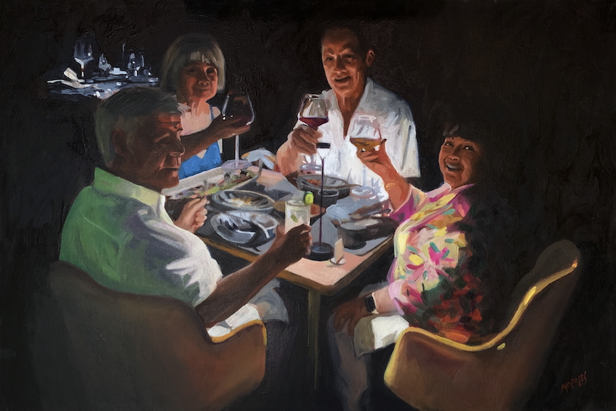 Grupo de cuatro personas sonriendo y brindando con copas en una mesa iluminada, rodeados de platos y vasos, en un ambiente acogedor y festivo.