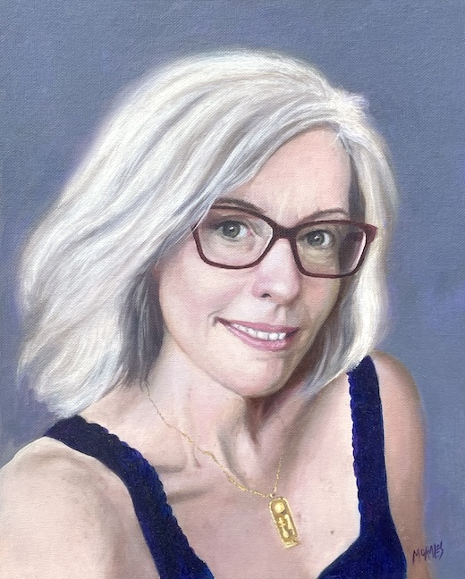 Retrato de una mujer con cabello rubio platino y gafas, sonriendo. Lleva una blusa negra y un collar dorado, con un fondo gris suave.